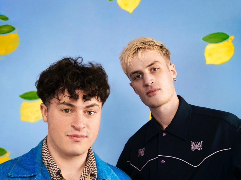 Both members of Kawala staring at the camera with a wall of lemons in the background