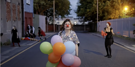 Beija Flo walking down a street with a clown nose on and holding numerous coloured balloons