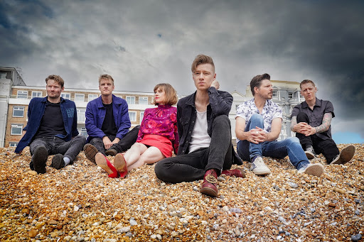 Skinny Lister band members sitting on a stony beach
