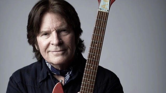 John Fogerty holding a guitar and wearing a neckerchief