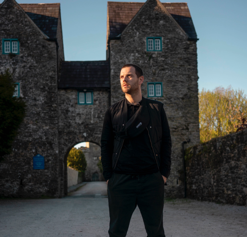 Mike Skinner from the streets standing with his hands in his pockets outside an old mansion