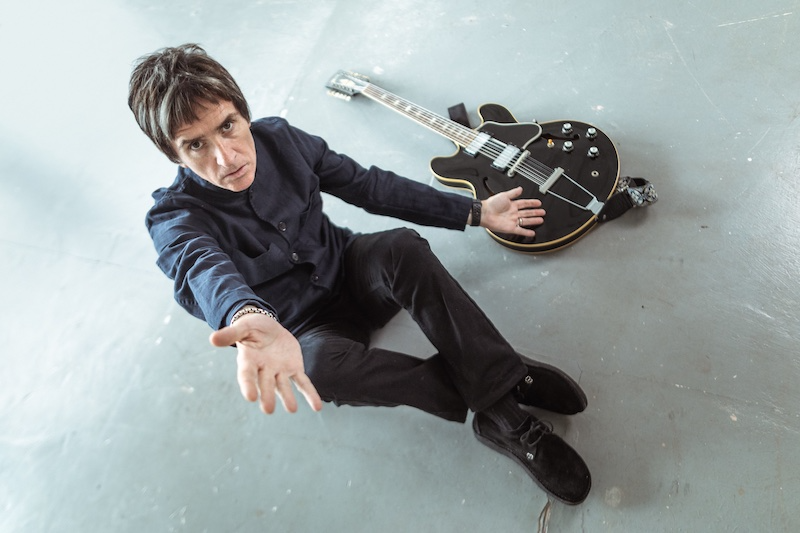 Johnny Marr sat on the floor next to a guitar with his hand out