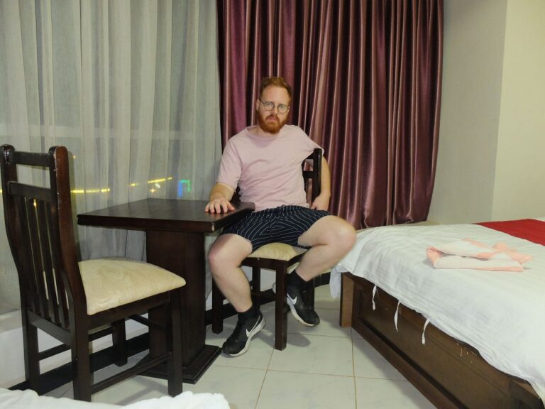 Sean at the hotel sitting in a hotel room with a t-shirt and boxer shorts on next to a bed