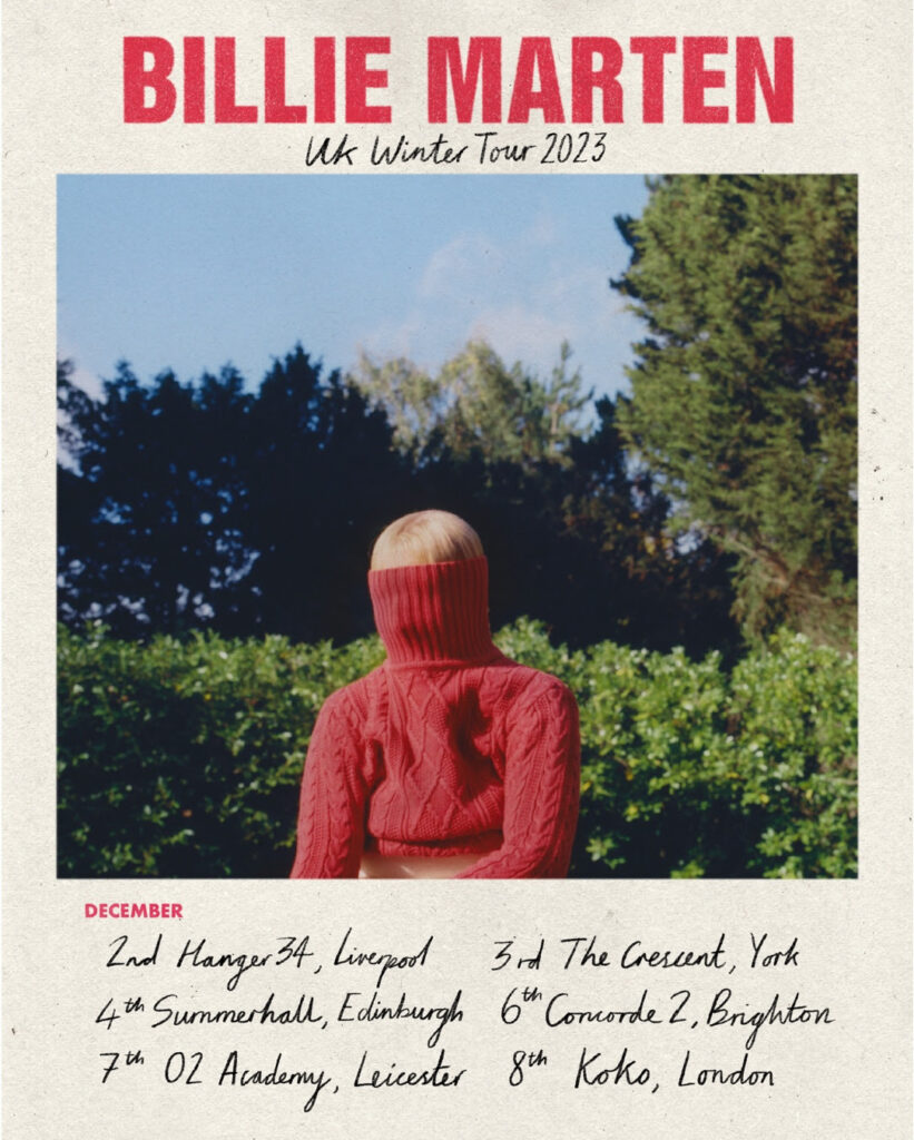 Billie Marten with a red jumper over her face sitting in front of trees