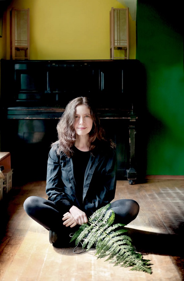 Sarah McQuaid sitting on a wooden floor in front of a piano with a large leaf in her hand
