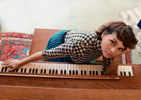 Norah Jones leaning on a piano keyboard looking up