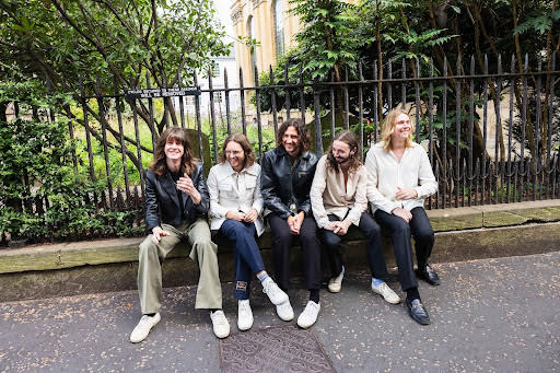 Blossoms band sitting on a very low wall with a fence behind them