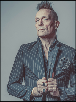 John Robb wearing a pin strip jacket and holding it closed with his hands