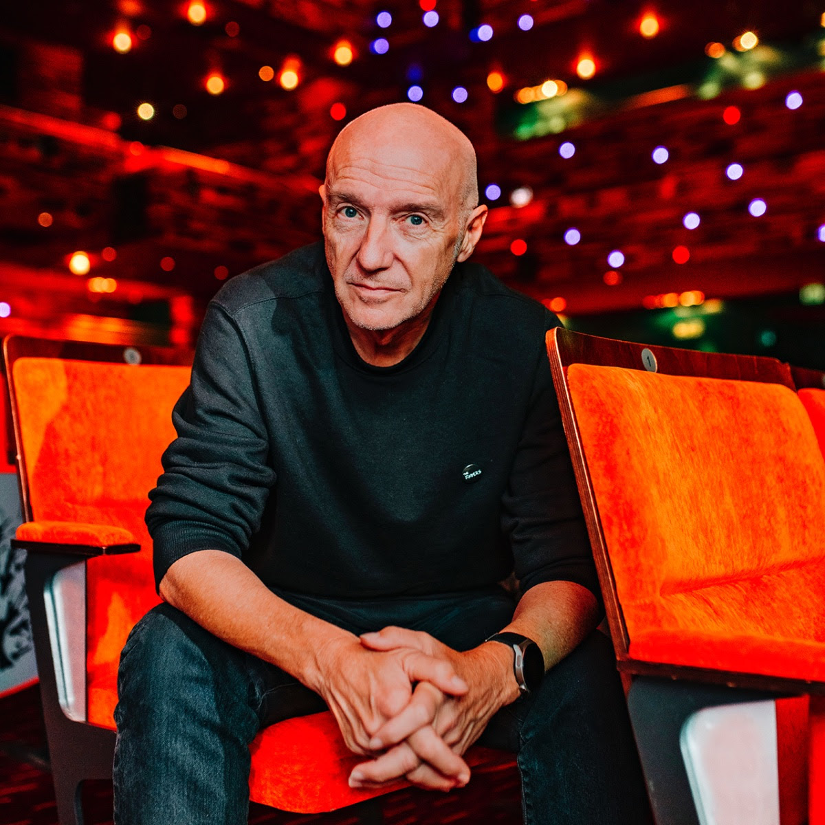 Midge Ure sitting in a red chair in an arena