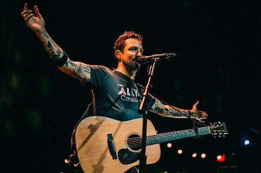 Frank turner onstage with his arms outstretched and a guitar around him