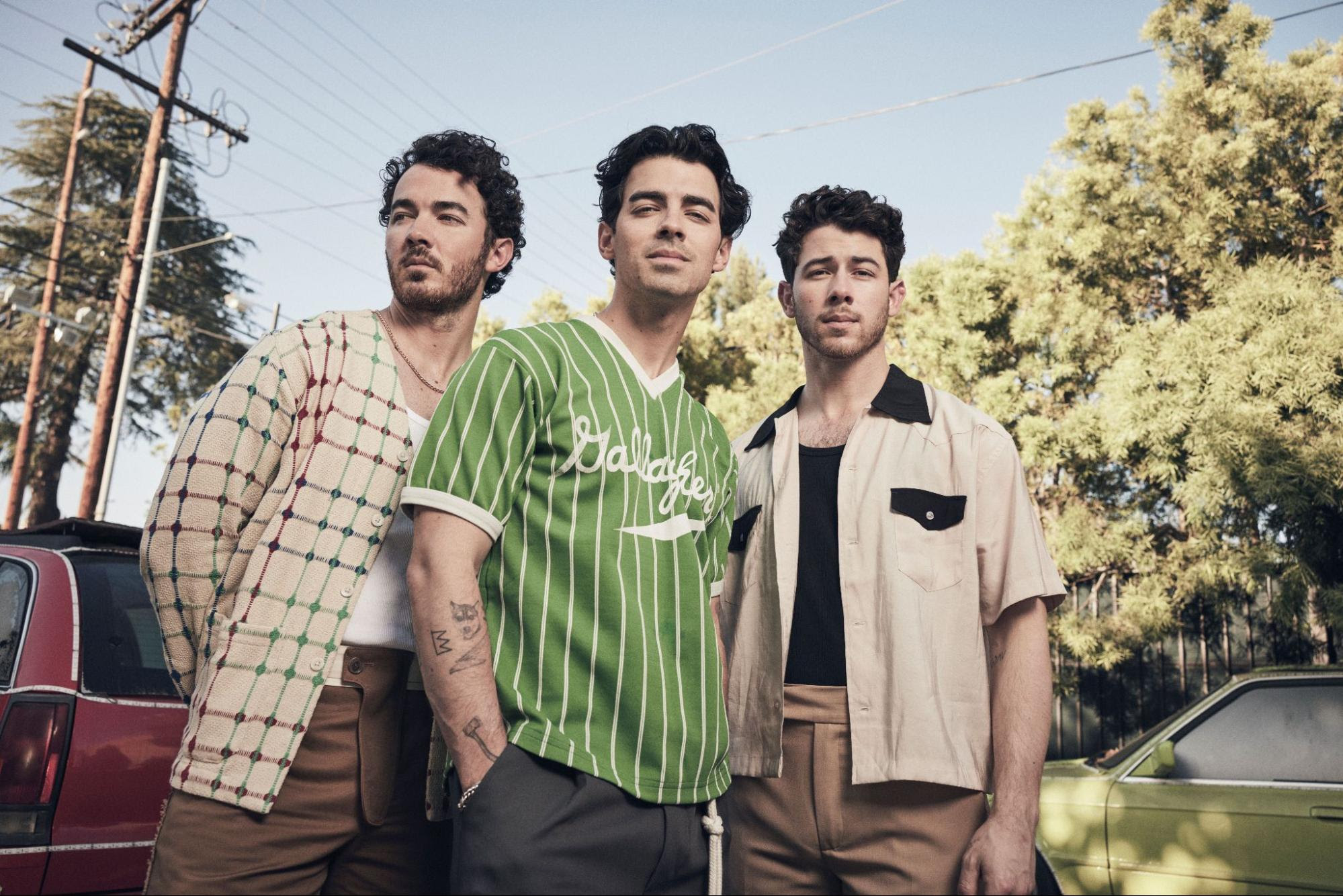 Jonas Brothers stood by some cars with trees in the background