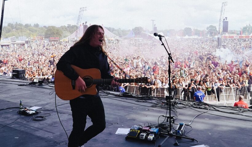 Jamie webster on stage at a festival with his guitar