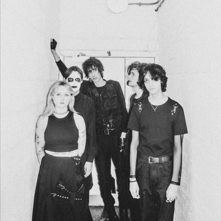 Black and white photo of the horrors stood in a corridor with a door behind them
