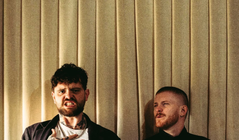 Big special stood in front of some blinds grimacing