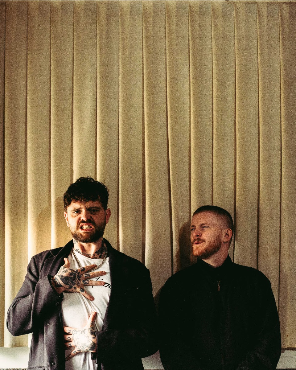 Big special stood in front of some blinds grimacing