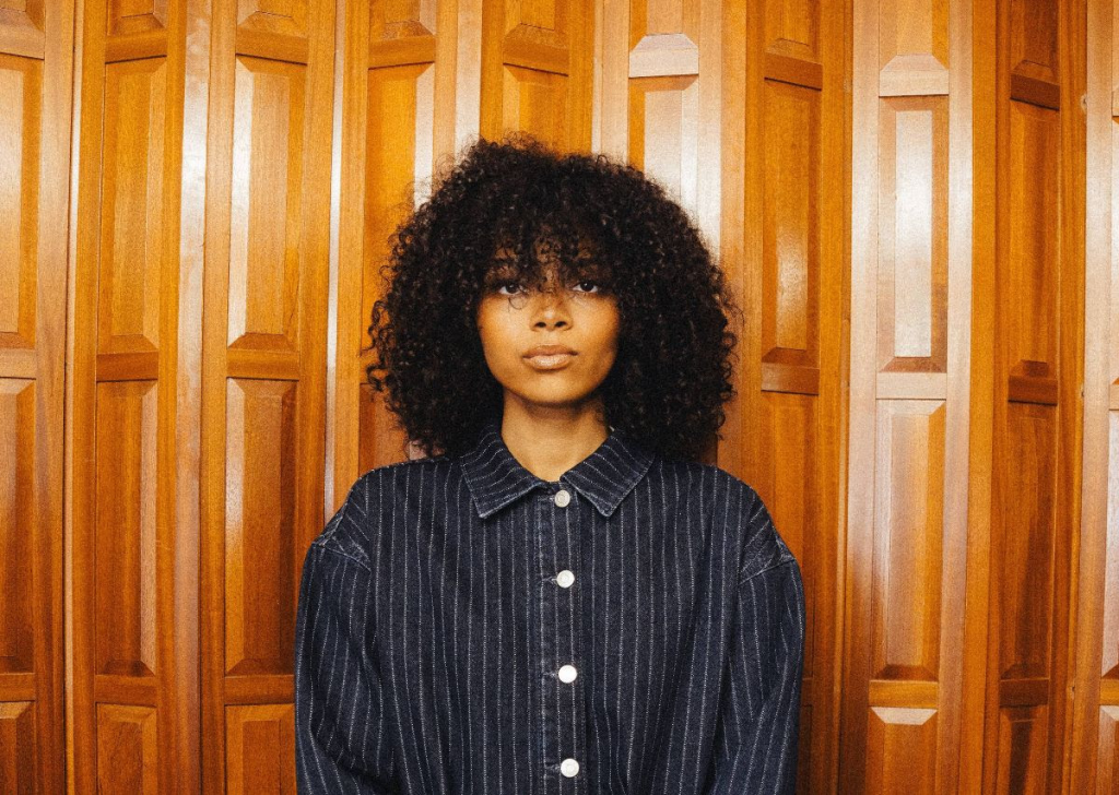 Brooke Combe stood in front of a wooden background in a striped shirt