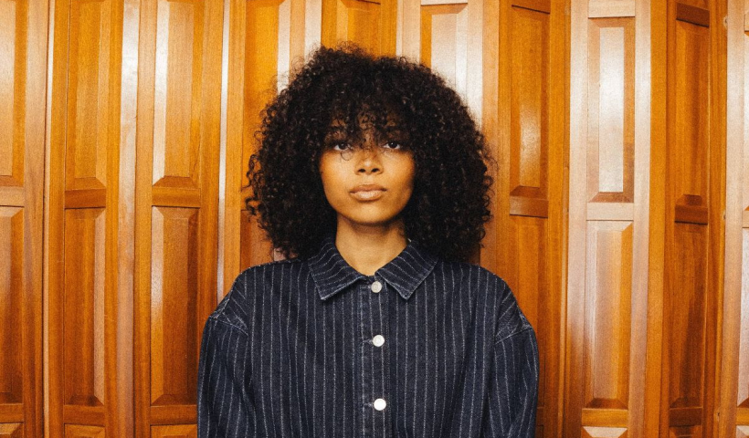 Brooke Combe stood in front of a wooden background in a striped shirt