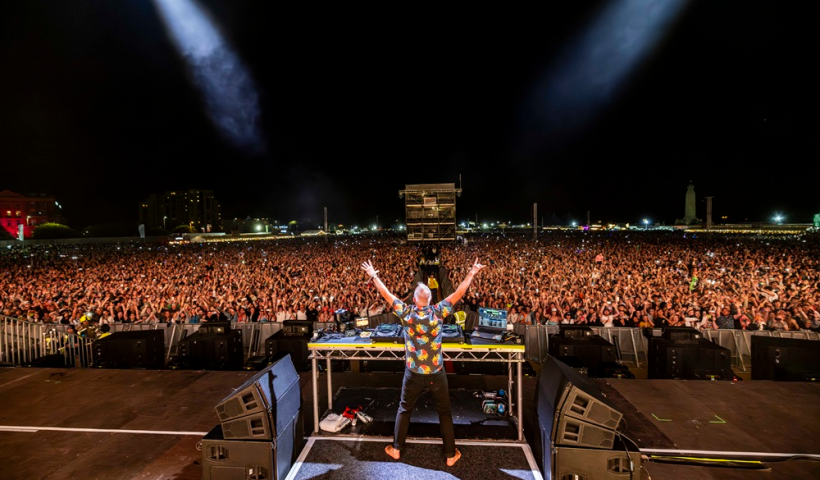 Photo of fatboy slim from behind with his arms raised in front of thousands of people