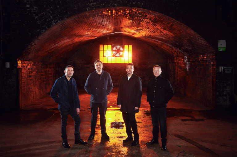 Starsailor standing in an underground venue with a bright yellow light behind them