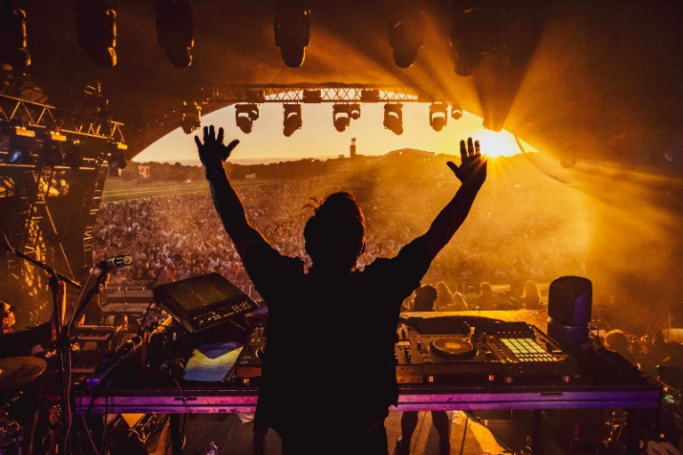 Pete tong with his arms raised on stage with the crowd in front of him