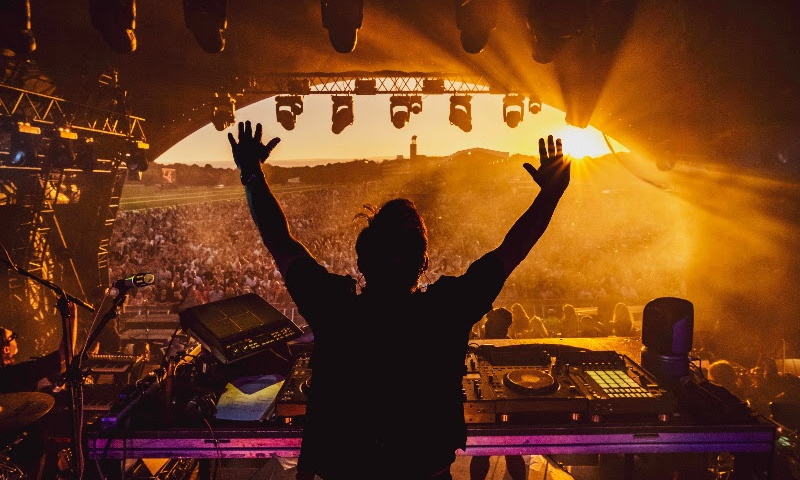 Pete tong with his arms raised on stage with the crowd in front of him