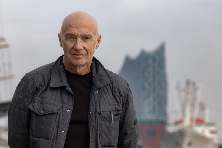 Midge Ure in front of a large building which is in the background