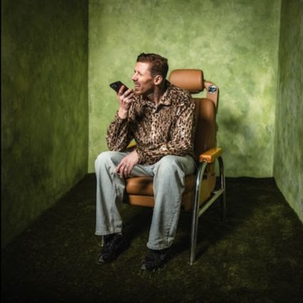 Professor Green sitting in a chair talking on his phone